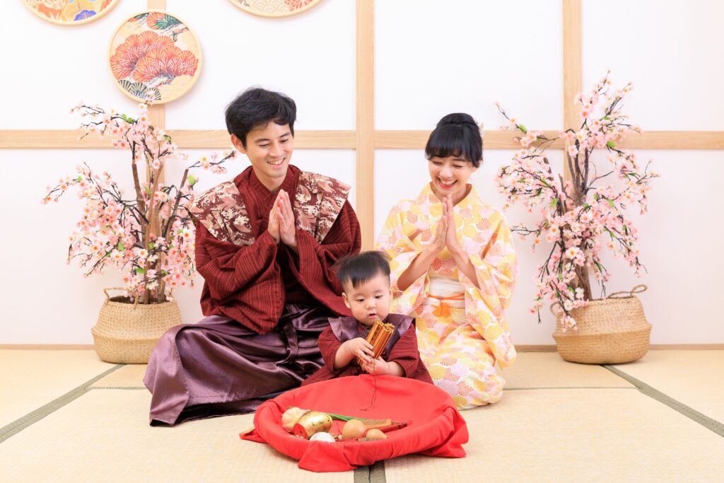 穿著日式和服的父母與寶寶參與抓周儀式,寶寶手持象徵未來的物品,周圍擺放傳統抓周道具,背景點綴櫻花與日式裝飾,展現溫馨家庭氛圍與傳統文化的融合。