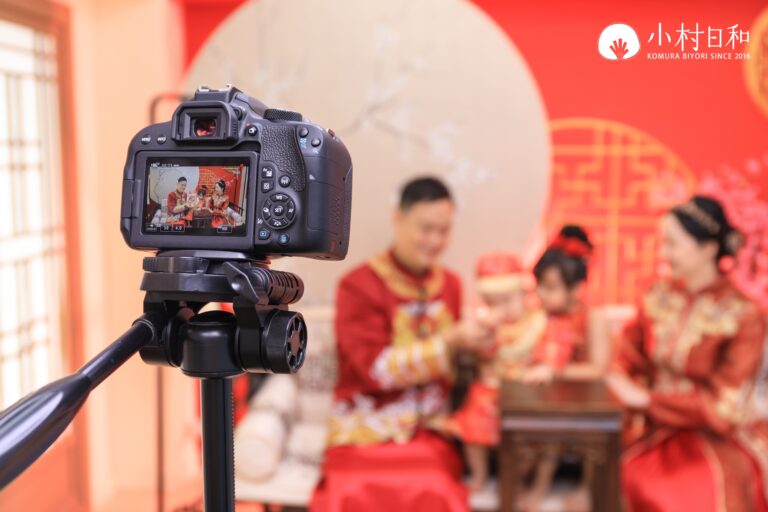 攝影機鏡頭對準正在進行抓周儀式的家庭，攝影機畫面清晰地捕捉家庭互動，背景為鮮紅的中式佈景。