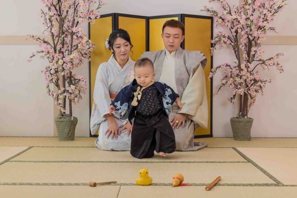 寶寶穿著日式武士風服飾，在榻榻米上向前爬行選擇抓周道具，背後的父母笑著注視，見證珍貴的成長時刻。
