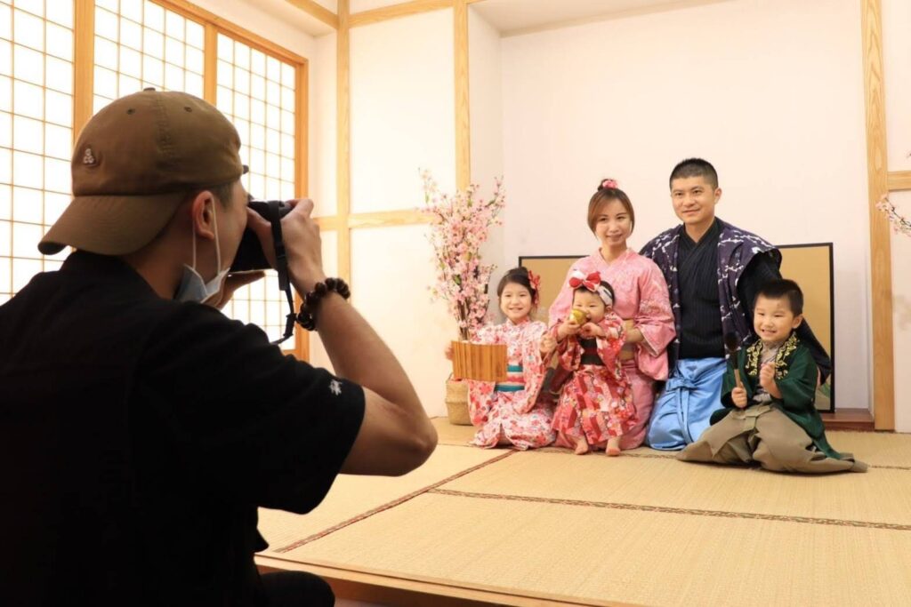 攝影師在日式場景中捕捉家庭抓周攝影畫面，一家人穿著傳統服飾，寶寶拿著抓周道具，畫面溫馨且充滿文化氛圍。