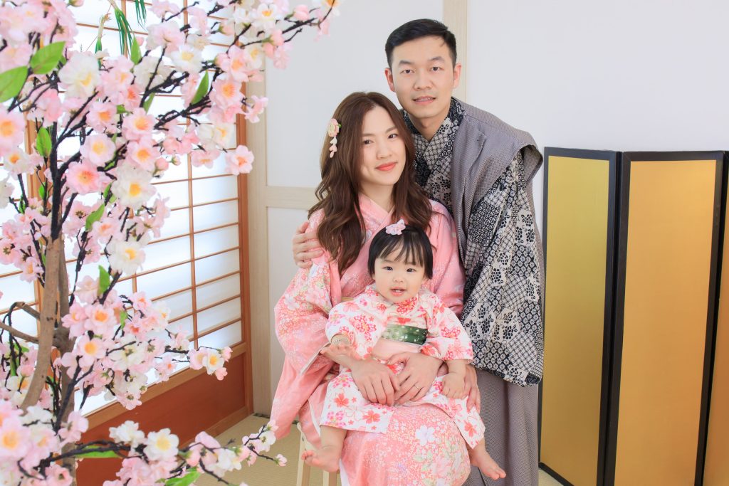一家三口穿著粉嫩色系日式和服，在櫻花棚景中拍攝全家福，氣氛溫馨自然。