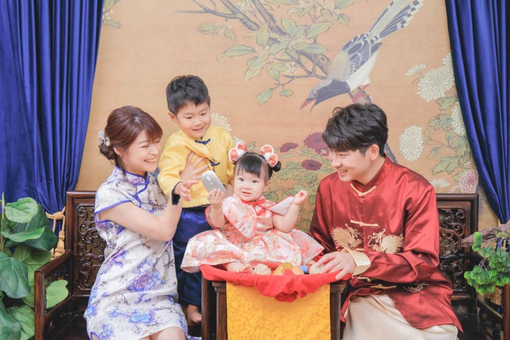 全家一起參與寶寶抓周儀式,寶寶坐在抓周椅上拿取道具,爸爸媽媽與哥哥穿著傳統服裝,溫馨記錄一歲成長時刻