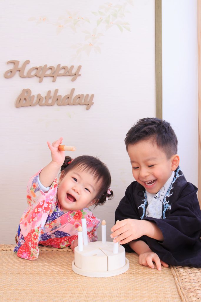 一歲寶寶抓周與生日紀念照,兄妹一起玩抓周道具,背景為 Happy Birthday 佈置,記錄寶寶的重要成長儀式