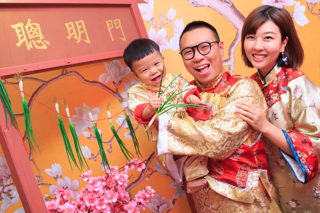 寶寶穿著中式抓周服飾開心摸蔥門,象徵智慧與好兆頭的抓周儀式場景