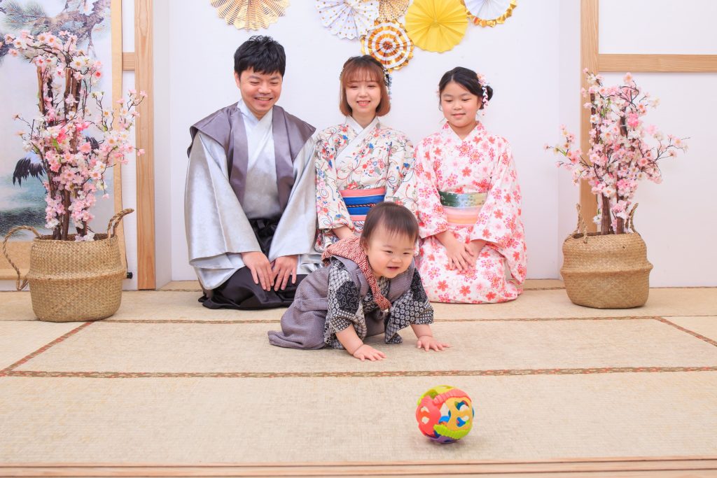 全家穿著和服圍坐,寶寶在榻榻米上開心爬行,準備要去抓眼前的球,溫馨親子互動瞬間。
