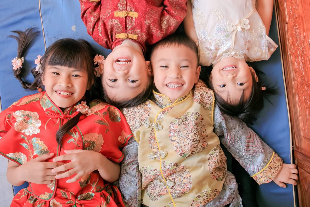 四個小朋友穿著中式傳統服裝，開心地躺在地上，展現童真的笑容。