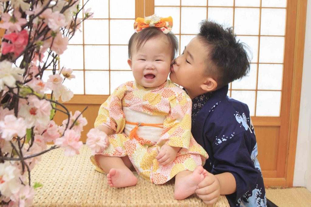 滿一歲寶寶穿日式和服開心微笑,哥哥溫柔親吻臉頰,櫻花場景溫馨合影。