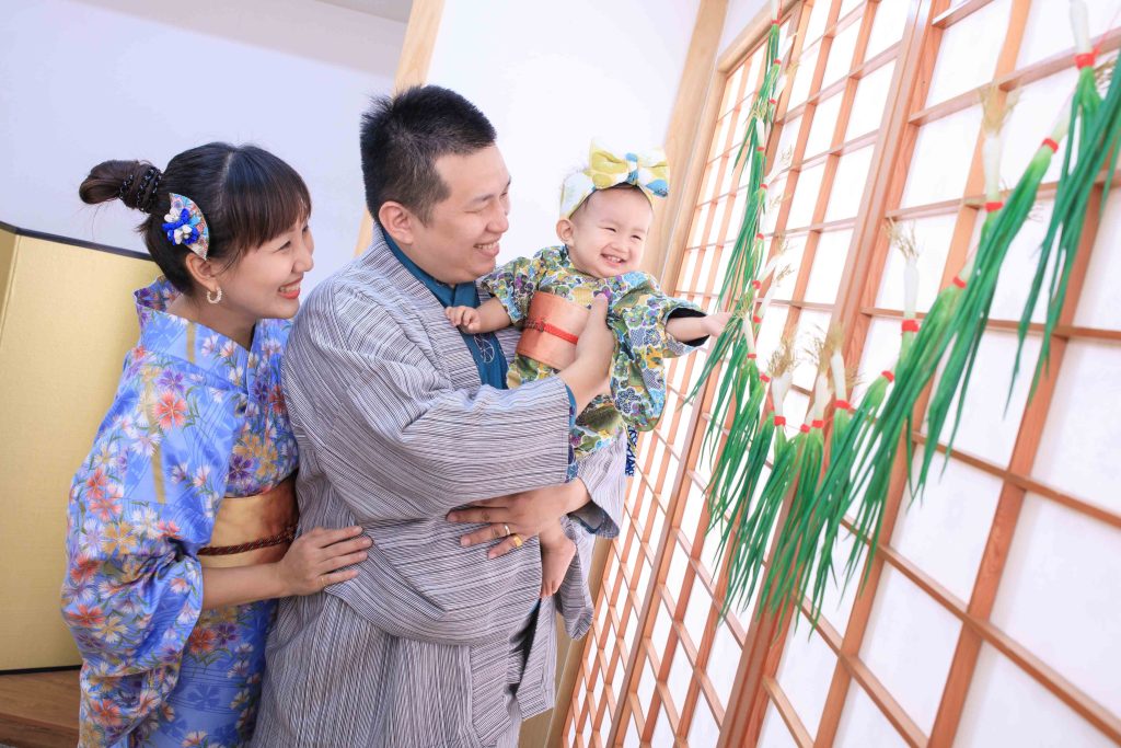 父母抱著寶寶參與摸蔥儀式,寶寶開心伸手觸摸蔥葉象徵聰明成長