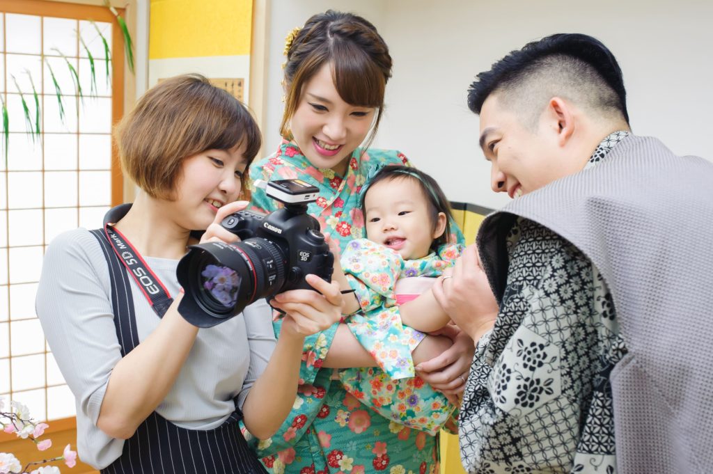 攝影師與父母一起查看相機畫面,寶寶穿著和服開心笑著,體驗專業抓周攝影的樂趣