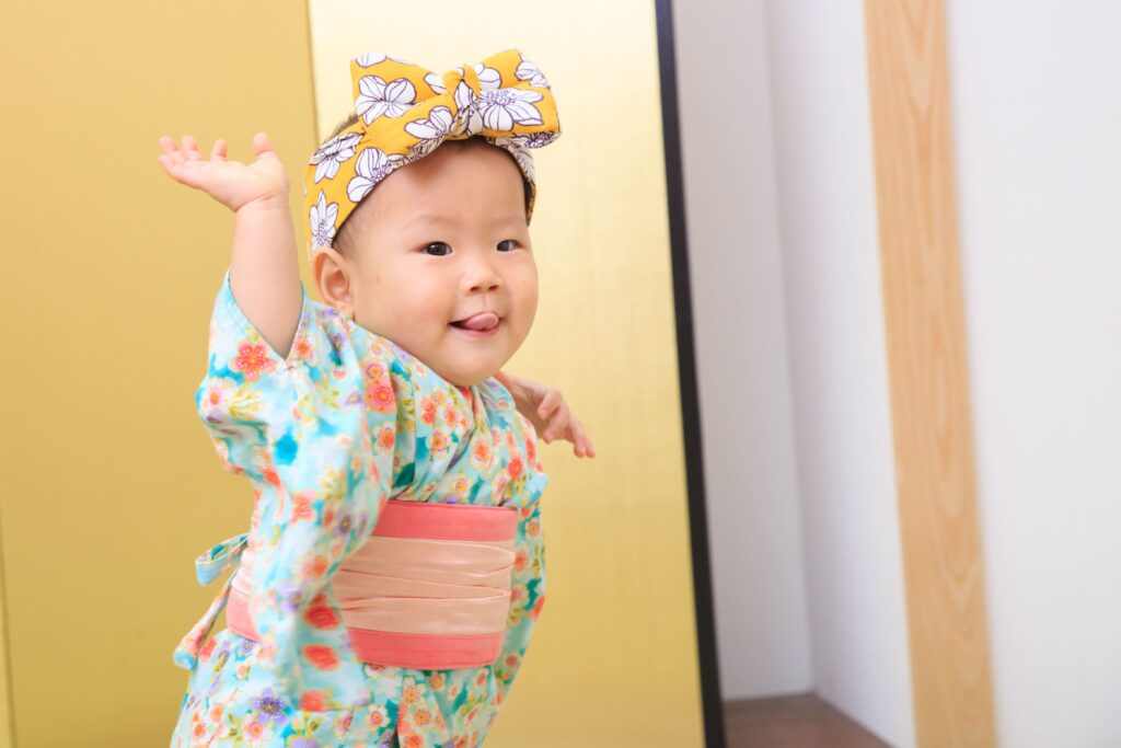 可愛的寶寶穿著日式和服，搭配大蝴蝶結頭飾，開心地擺出俏皮姿勢，拍攝於抓周攝影棚內。