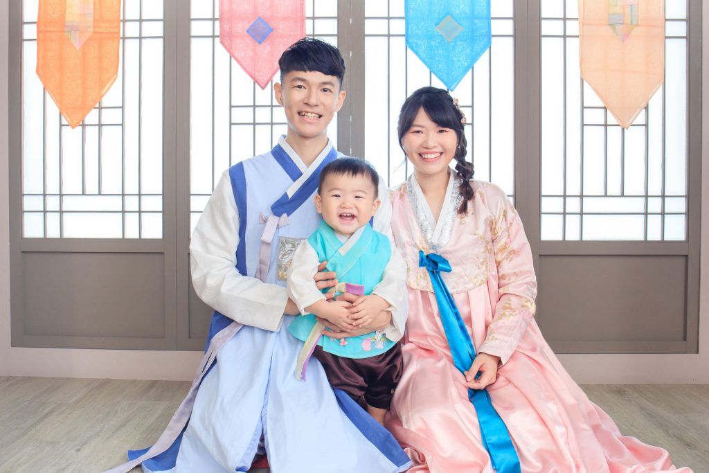 父母與寶寶穿著傳統韓服，在典雅韓式背景前展現幸福笑容。