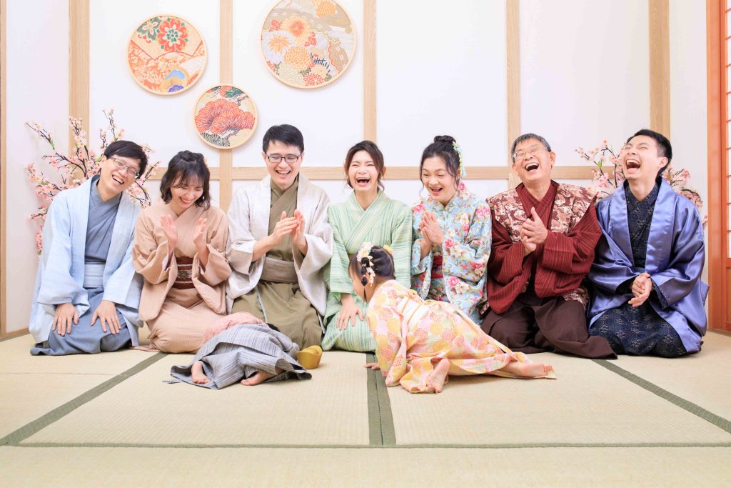 寶寶抓周儀式現場，家人穿傳統和服圍坐拍手歡笑，寶寶在榻榻米上爬行進行背餅儀式