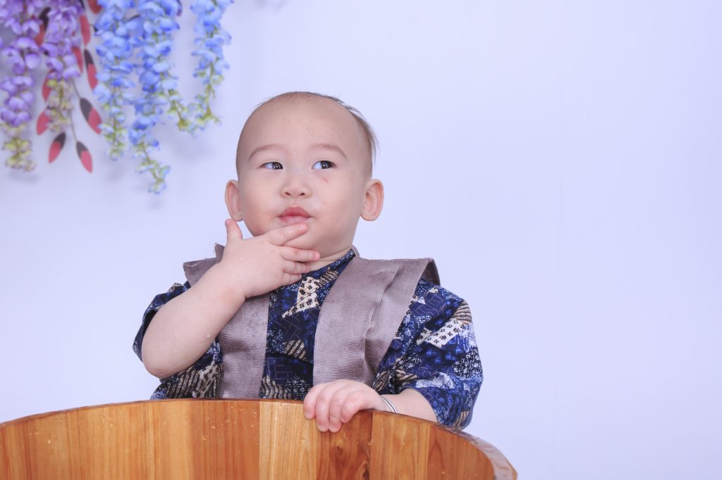 寶寶抓周拍攝現場,小男嬰穿著藍色傳統服裝坐在木桶中,呈現抓周儀式自然互動畫面