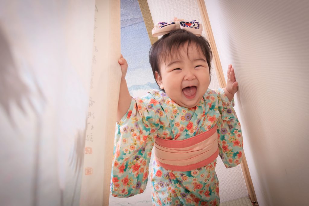 小女孩穿花紋和服，在日式屏風場景中扶著牆面開心大笑