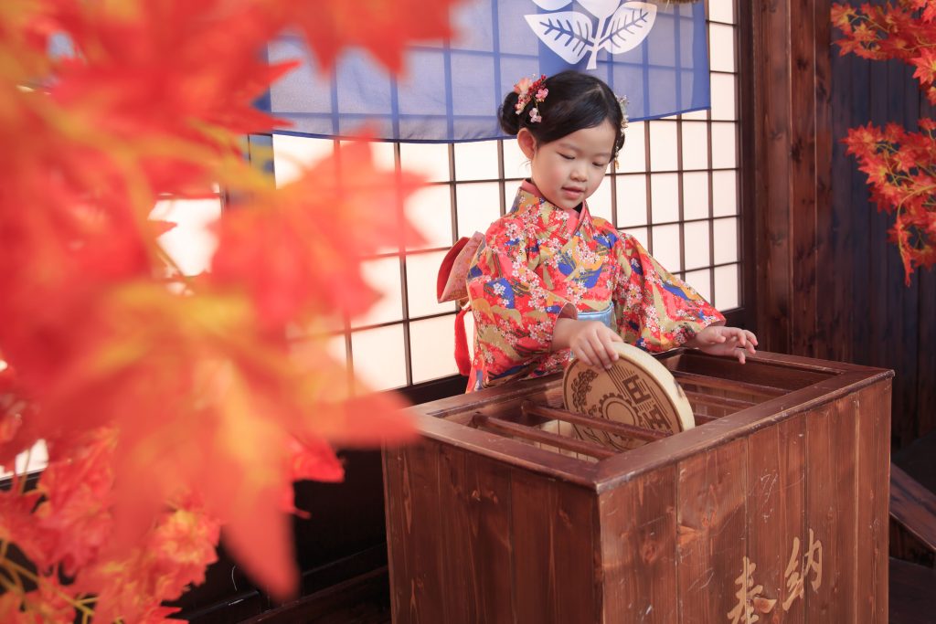 小女孩穿紅色花紋和服，在日式木製賽錢箱中投取有諧音為御緣的5日圓硬幣